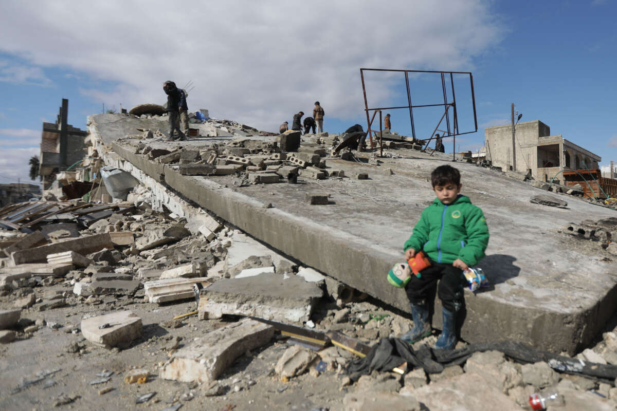 A Syrian child sits on a collapsed building after the deadly earthquake