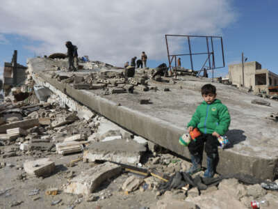 A Syrian child sits on a collapsed building after the deadly earthquake