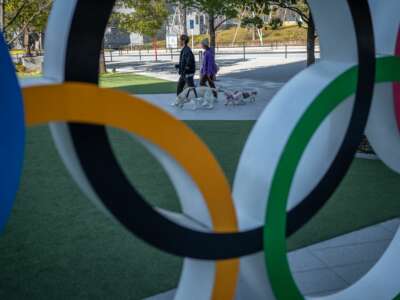 People walk their dogs past the Olympic rings near the National Stadium in Tokyo, Japan, on February 17, 2023.