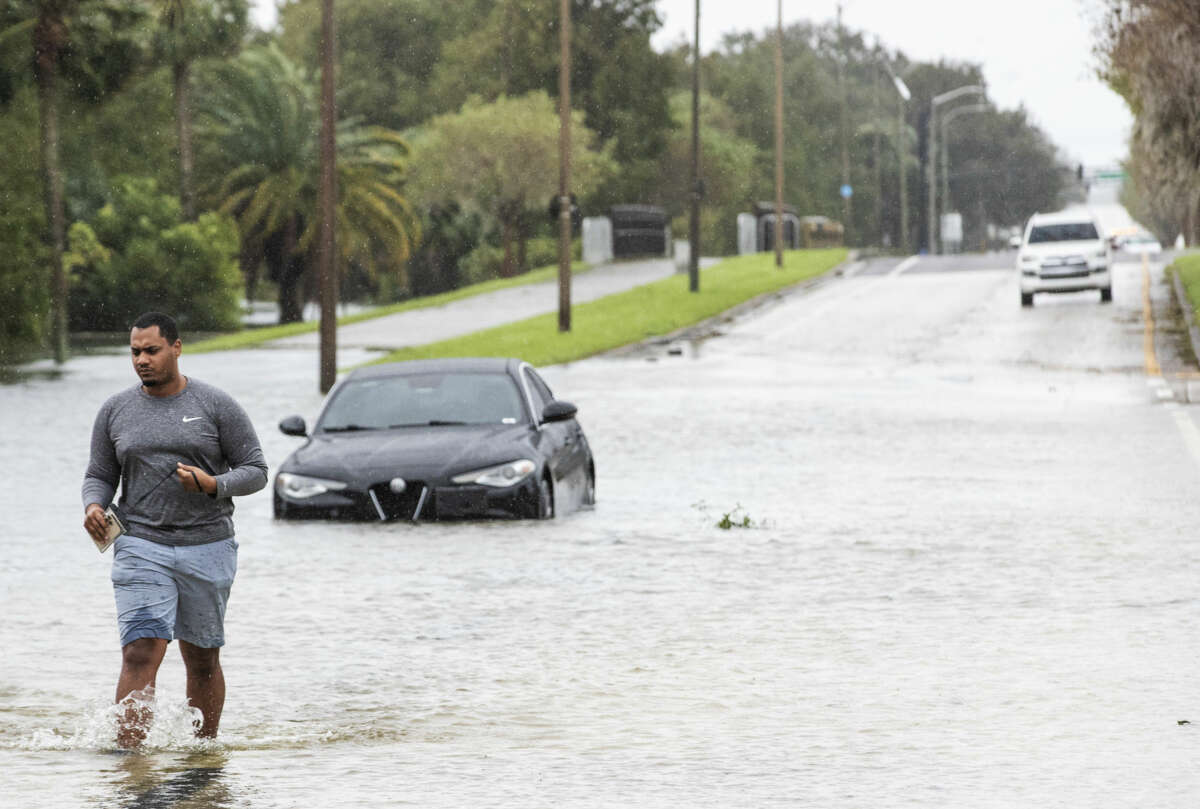 A man leaves his car behind to struggle through shin-deep floodwater