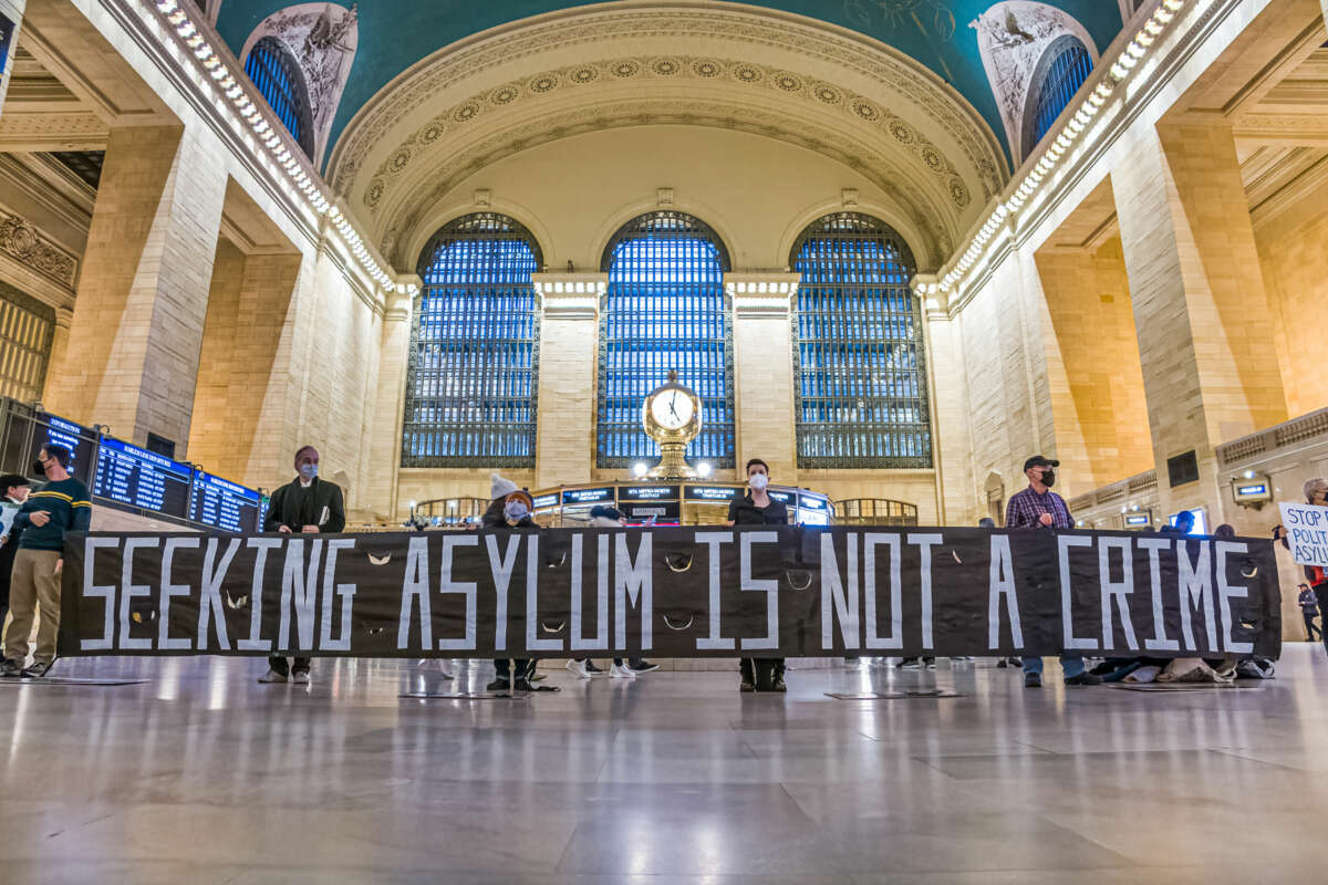 People display a banner reading "SEEKING ASYLUM IS NOT A CRIME" during a protest inside of a train station