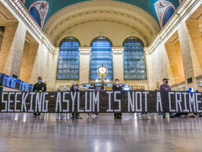 People display a banner reading "SEEKING ASYLUM IS NOT A CRIME" during a protest inside of a train station