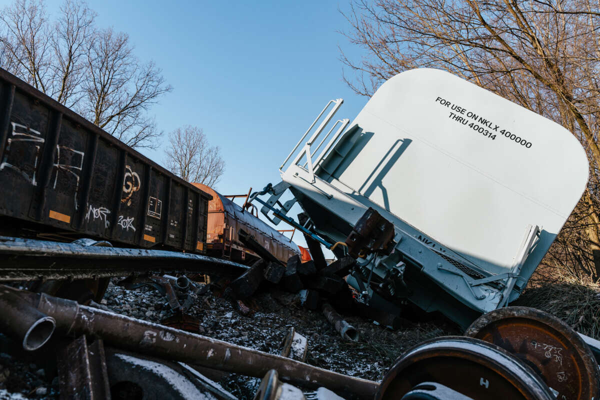 A Norfolk Southern train is seen derailed and laying on its side beside the tracks