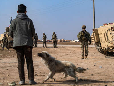 A young boy accompanied by a dog stares at U.S. soldiers as a convoy patrols the area near the town of Tell Hamis, southeast of the city of Qameshli in Syria’s northeastern Hasakeh Governorate, on January 26, 2023.