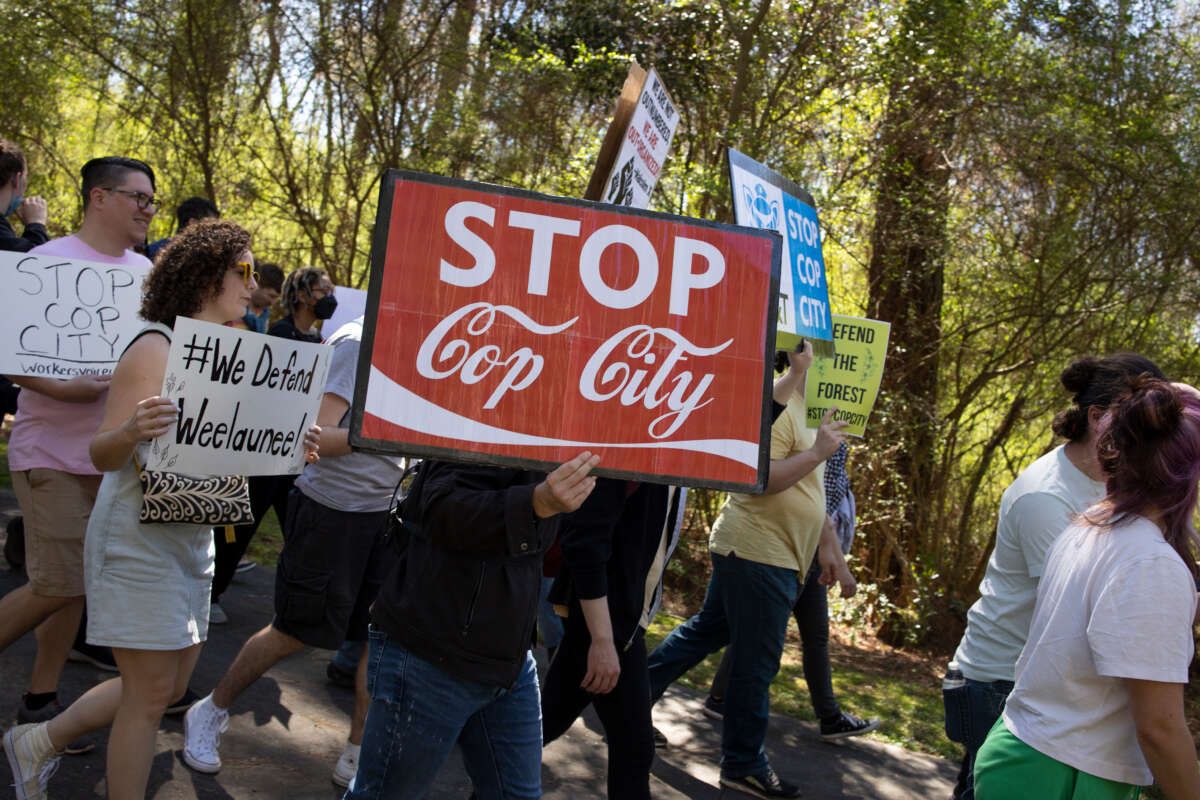 Environmental activists march through a preserved forest that is scheduled to be developed as a police training center, March 4, 2023, in Atlanta, Georgia, with sign reading 'stop cop city'