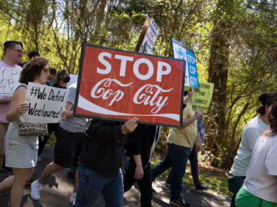 Environmental activists march through a preserved forest that is scheduled to be developed as a police training center, March 4, 2023, in Atlanta, Georgia, with sign reading 'stop cop city'