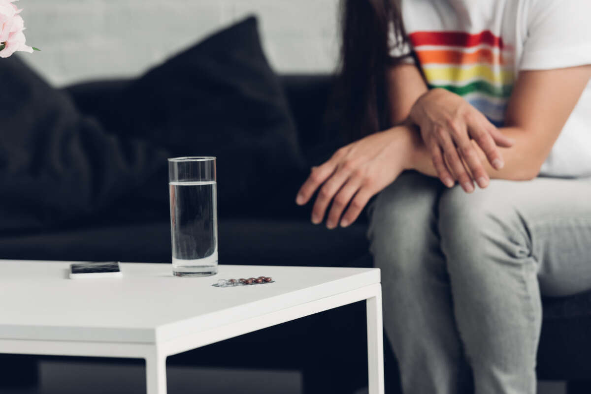 Cropped shot of man in t-shirt with pride flag sitting in front of glass of water and pill.