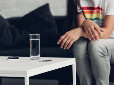 Cropped shot of man in t-shirt with pride flag sitting in front of glass of water and pill.