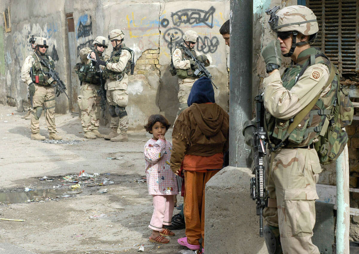 U.S. soldiers patrol Baghdad street as a young Iraqi girl looks on