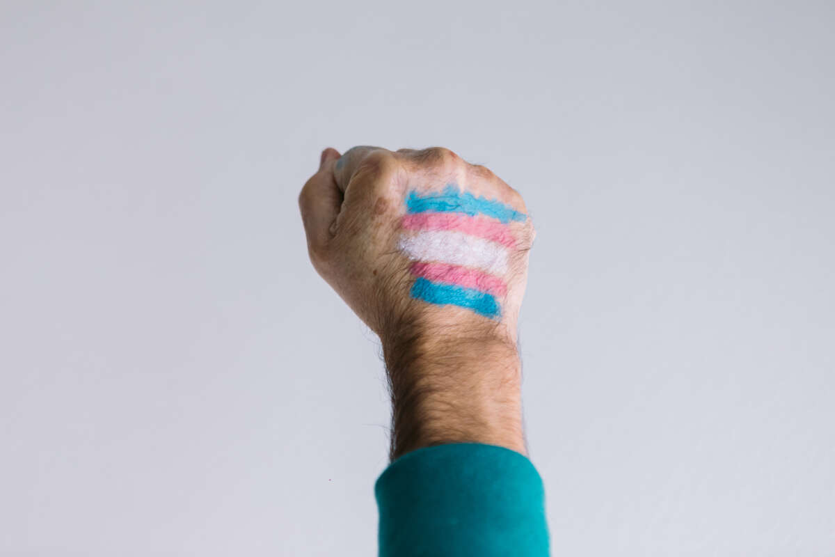 A raised, clenched fist is pictured with a trans flag painted on it.