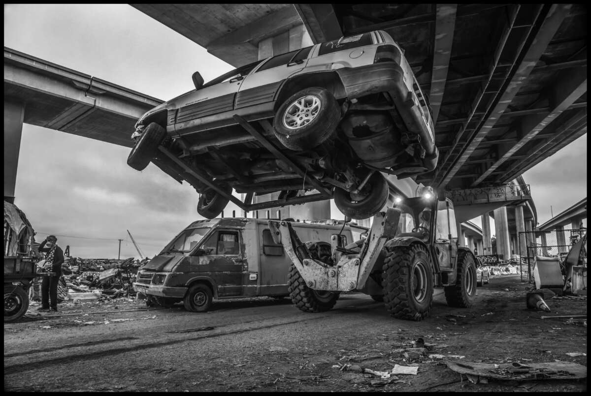 As a resident watches, a forklift hoists a resident's SUV and takes it out of the camp under the freeway.