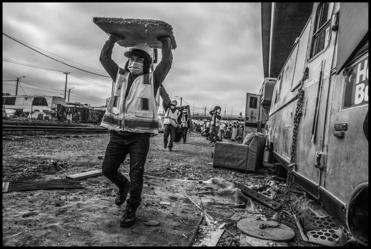 Day laborers in long lines bring items to the dumpster to be trashed.