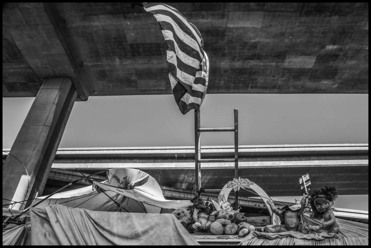 Dolls and a flag are ironic comments left on a vehicle under the freeway, about to be towed away.