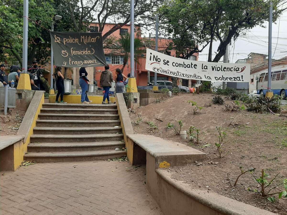 People standing on stairs display banners in Spanish that, when translated, read "the military police are femicidal and trans-hating" and "Violence is not battled by criminalizing poverty!"