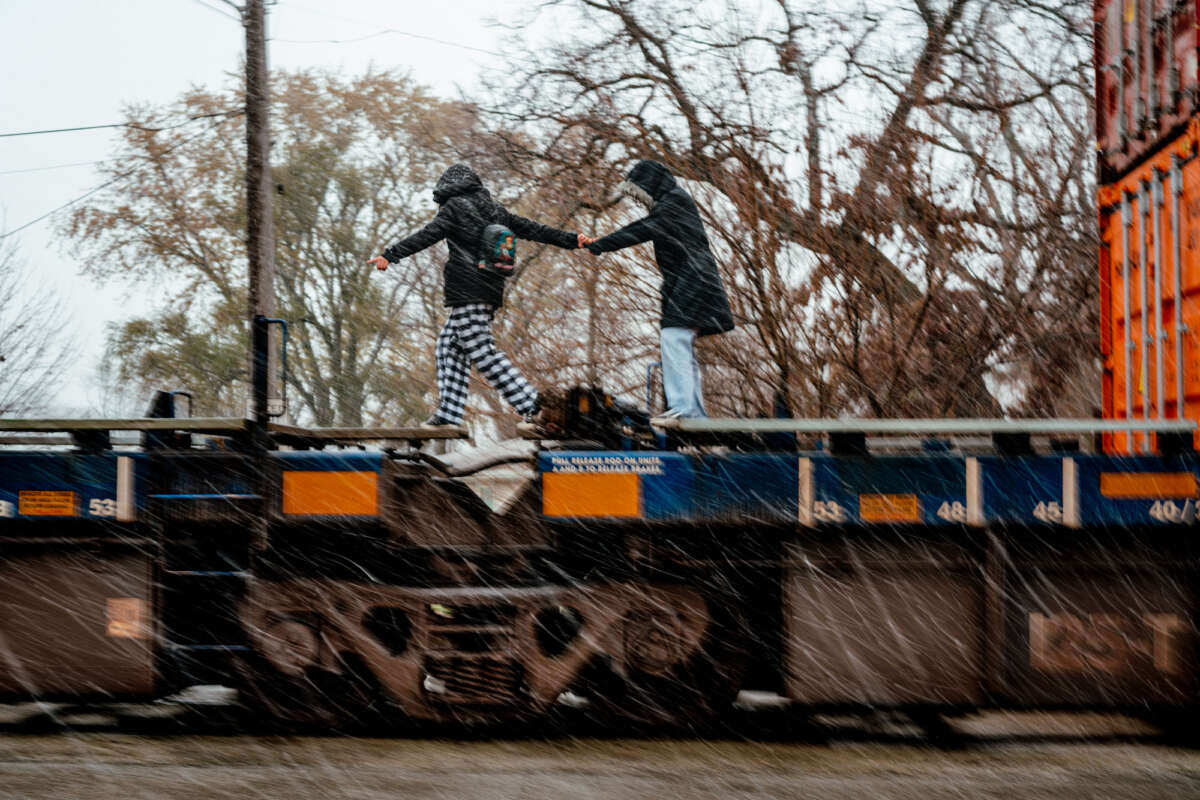 Two children on their way to school help each other over a parked train.