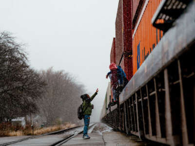 One child helps another cross over a parked freight train blocking their route to school.