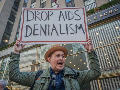 A man displays a sign reading "DROP AIDS DENIALISM" during an outdoor protest