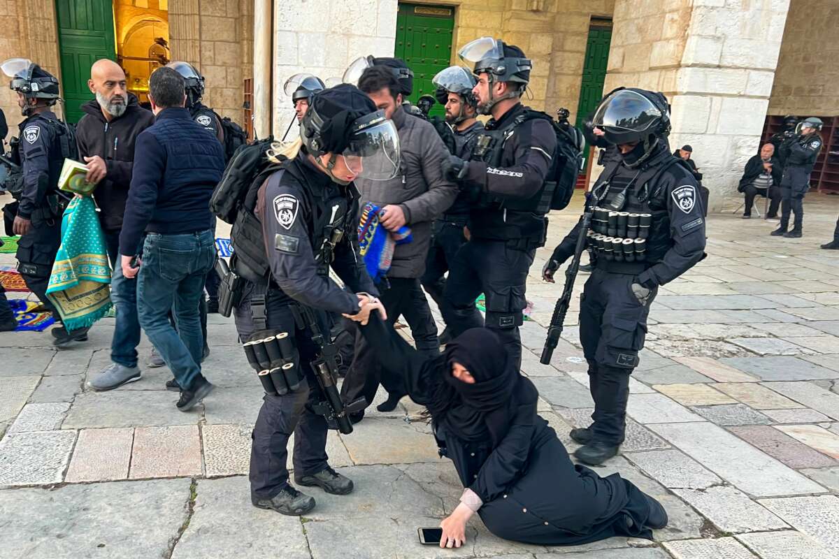 A praying woman in a hijab is dragged across the ground by armed members of the Israeli Defense Force