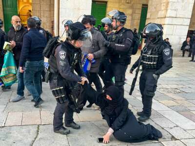 A praying woman in a hijab is dragged across the ground by armed members of the Israeli Defense Force