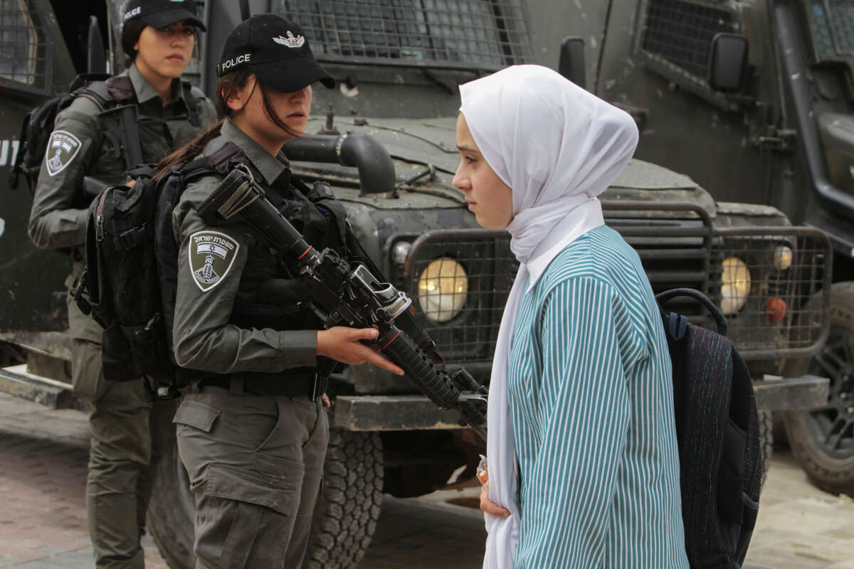 A girl in a hijab walks past Israeli Defense Force cops carrying automatic rifles