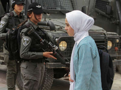 A girl in a hijab walks past Israeli Defense Force cops carrying automatic rifles