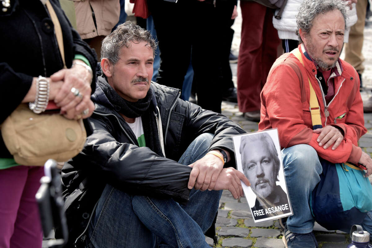 A man frowns while holding a sign of Julian Assange's face with a message of "FREE ASSANGE" printed beneath