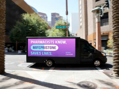 A truck with a video screen reading "PHARMACISTS KNOW, MIFERPRISTONE SAVES LIVES" drives through a city center