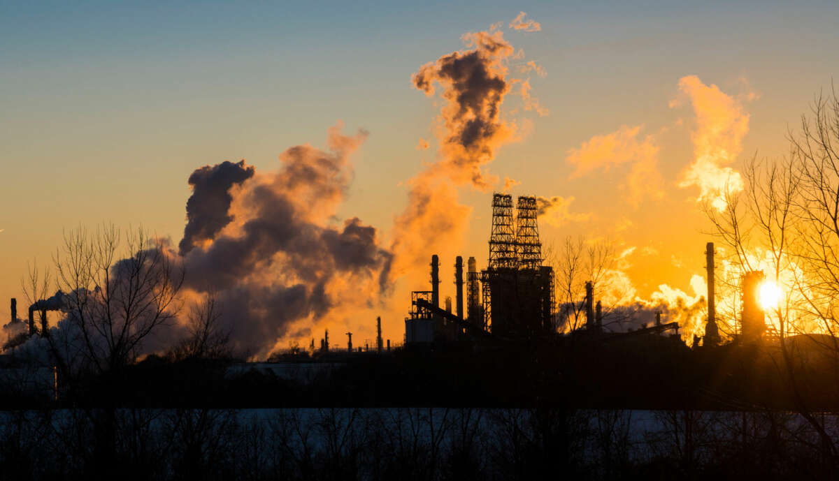 Smog rises from smokestacks against either a rising or setting sun