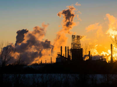 Smog rises from smokestacks against either a rising or setting sun