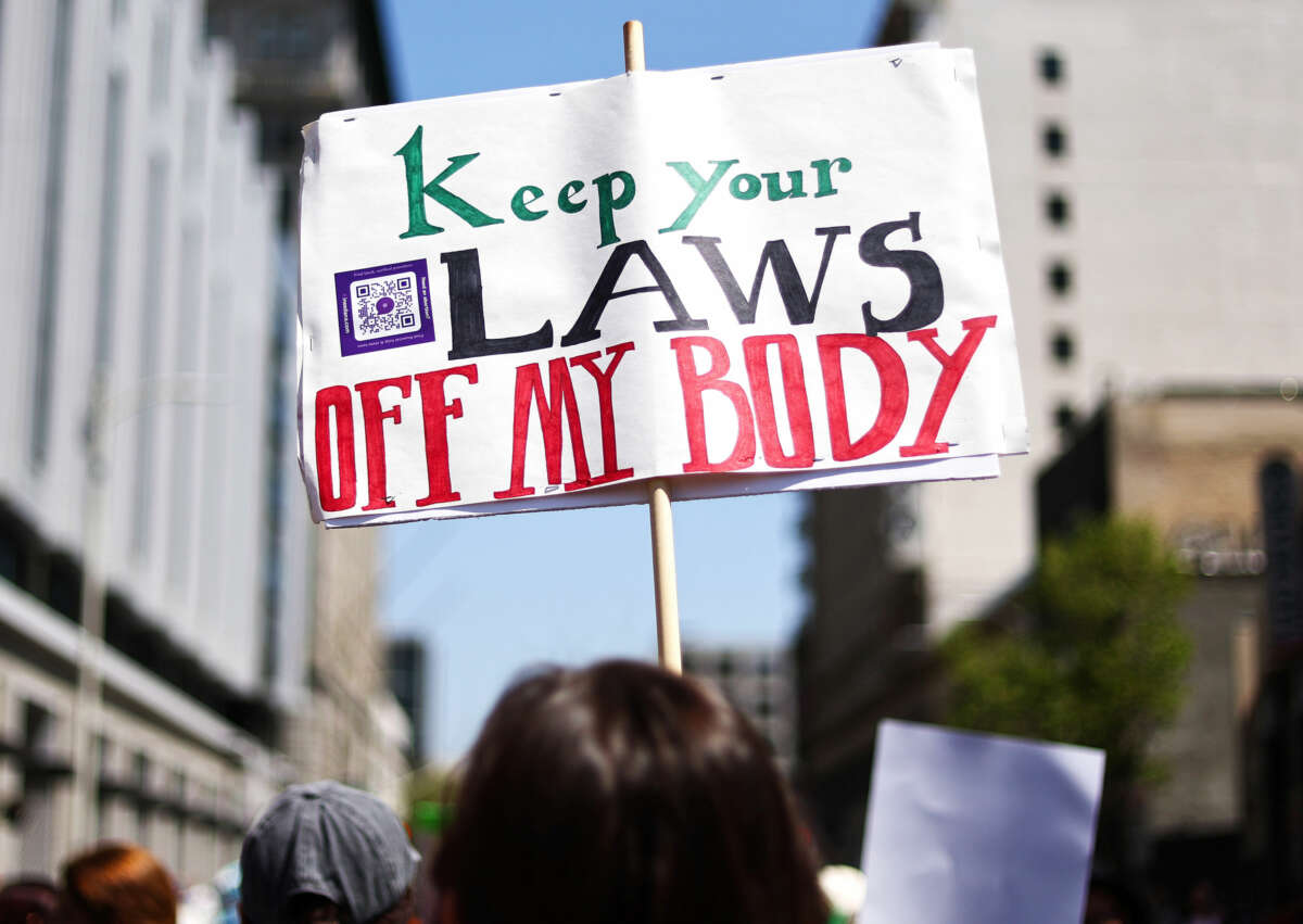 A protester holds a sign reading "KEEP YOUR LAWS OFF MY BODY" during an outdoor demonstration
