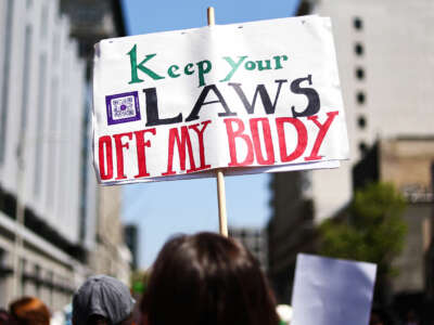 A protester holds a sign reading "KEEP YOUR LAWS OFF MY BODY" during an outdoor demonstration