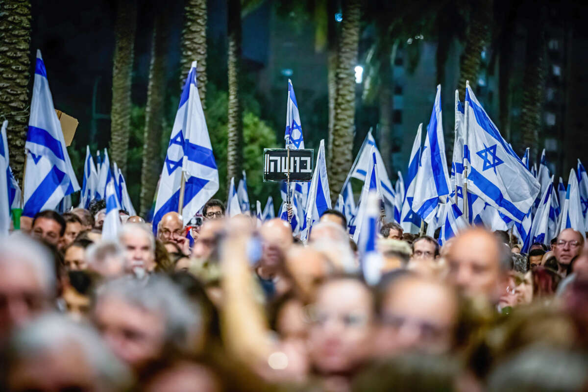 Israeli protestors hold flags and a placard in Hebrew that reads 'Shame' during an anti-government demonstration in the city of Netanya, north of Tel Aviv.