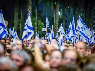 Israeli protestors hold flags and a placard in Hebrew that reads 'Shame' during an anti-government demonstration in the city of Netanya, north of Tel Aviv.