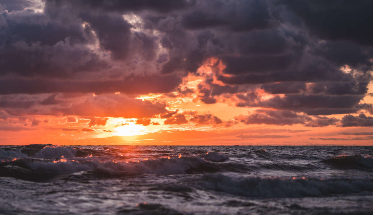 Sun setting over ocean horizon with dark clouds and choppy waters