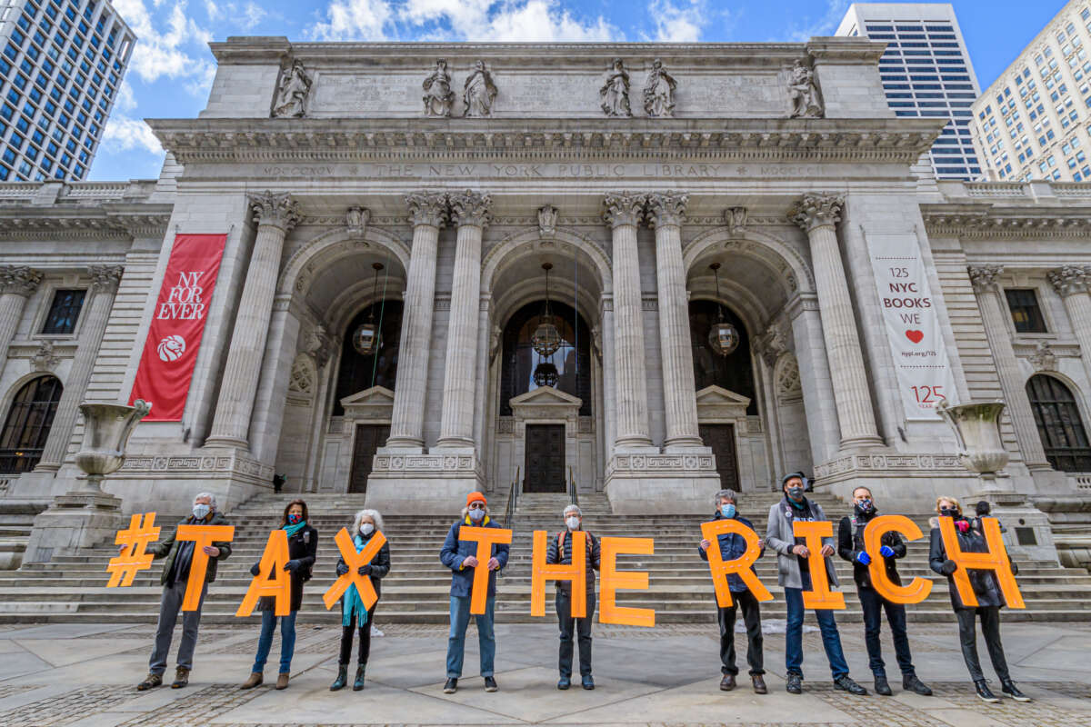 Protesters hold signs spelling out "Tax the Rich" outside the New York Public Library