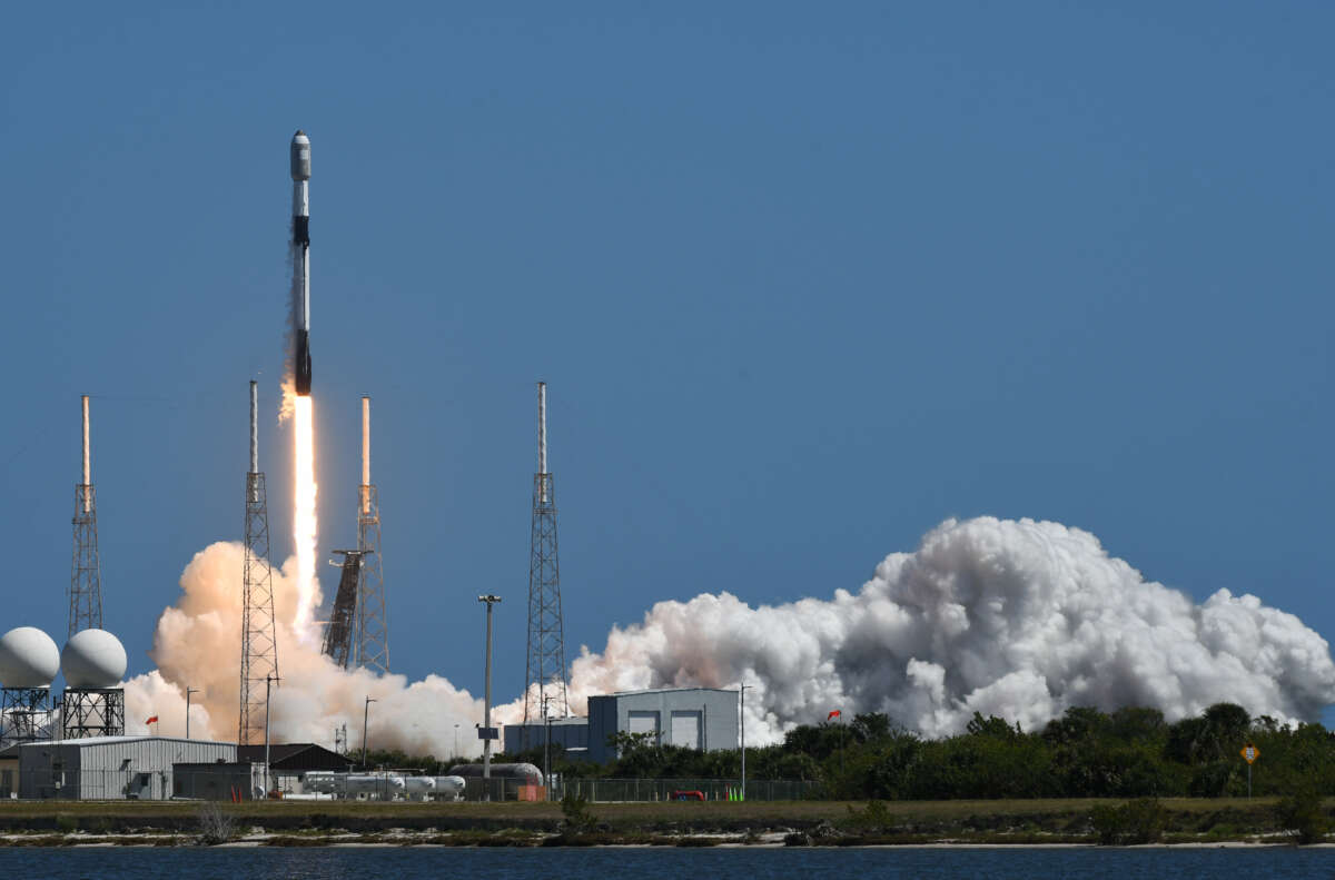 A rocket shoots into a blue sky, surrounded by clouds of smoke