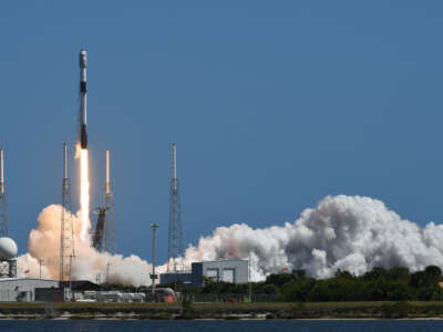 A rocket shoots into a blue sky, surrounded by clouds of smoke