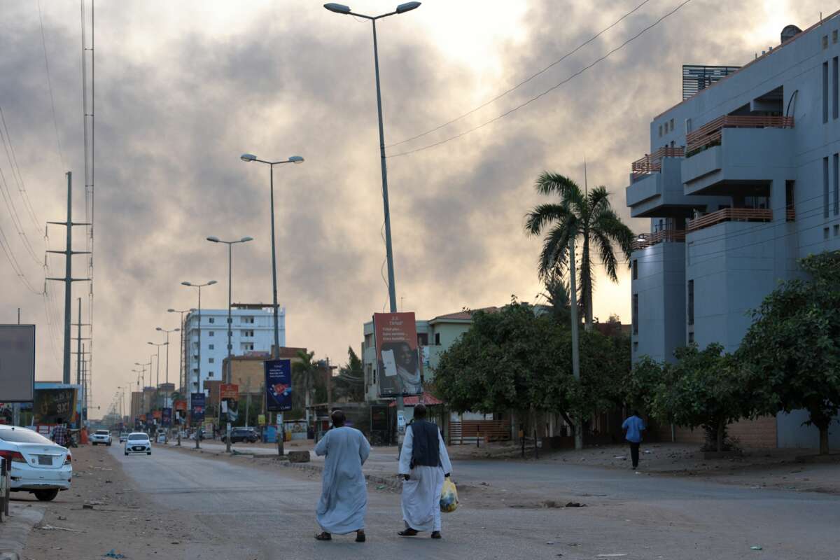 People walk along a street as smoke billows above buildings in Sudan