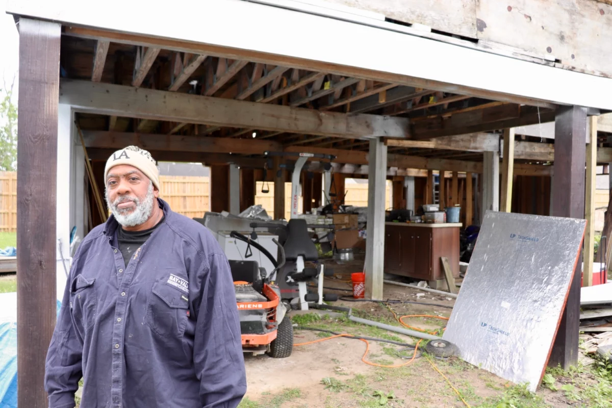 A Black man stands in front of a house that was damaged by Hurricane Ida