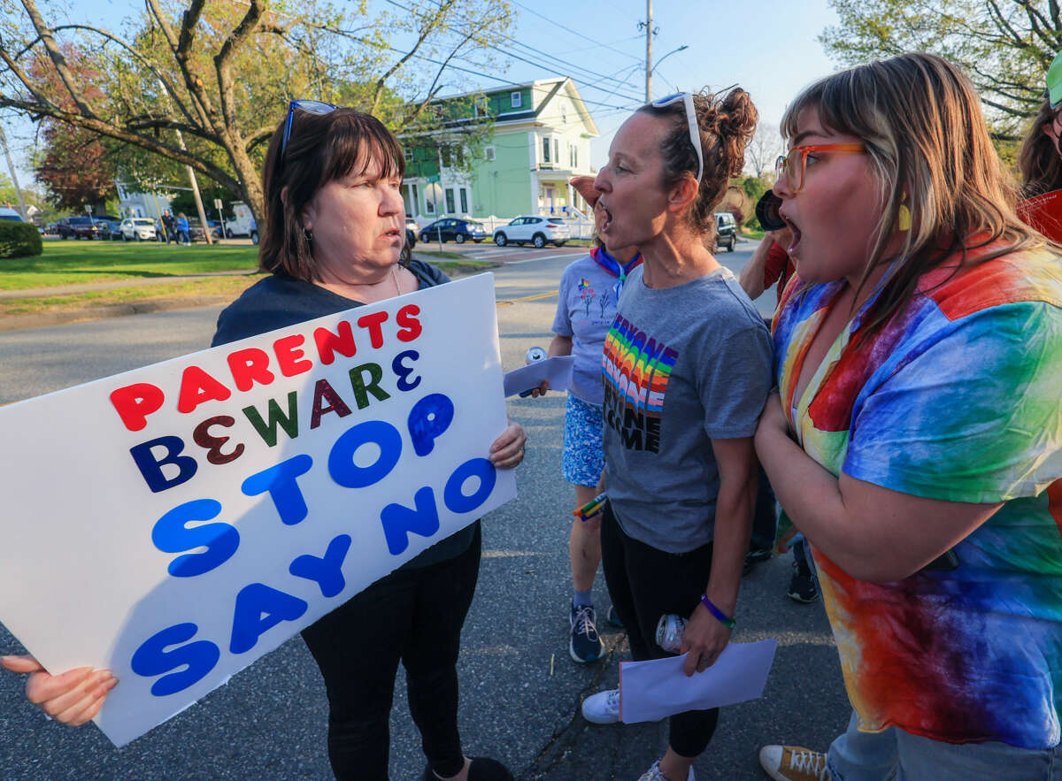 Two lgbtq+ allies speak with a woman holding a sign reading "PARENTS BEWARE STOP SAY NO"