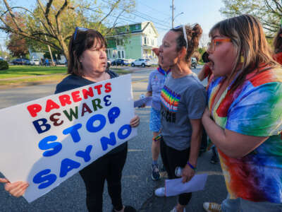 Two lgbtq+ allies speak with a woman holding a sign reading "PARENTS BEWARE STOP SAY NO"