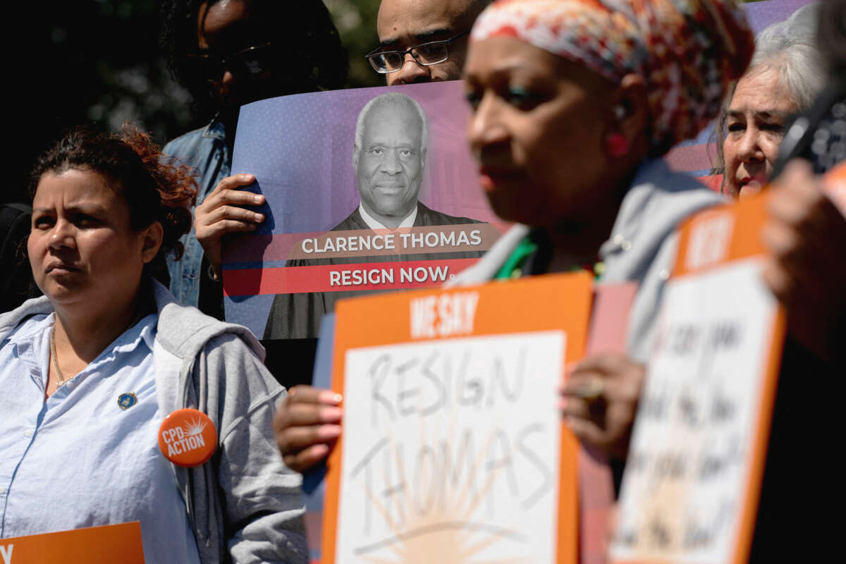 Protesters holding photos of Justice Clarence Thomas with calls for his resignation stand outdoors during a rally
