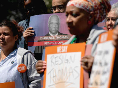 Protesters holding photos of Justice Clarence Thomas with calls for his resignation stand outdoors during a rally