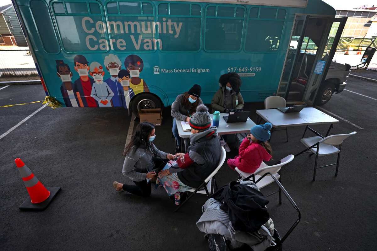 People receive aid in a parking lot outside of a teal van with the words "community care van" printed on the side