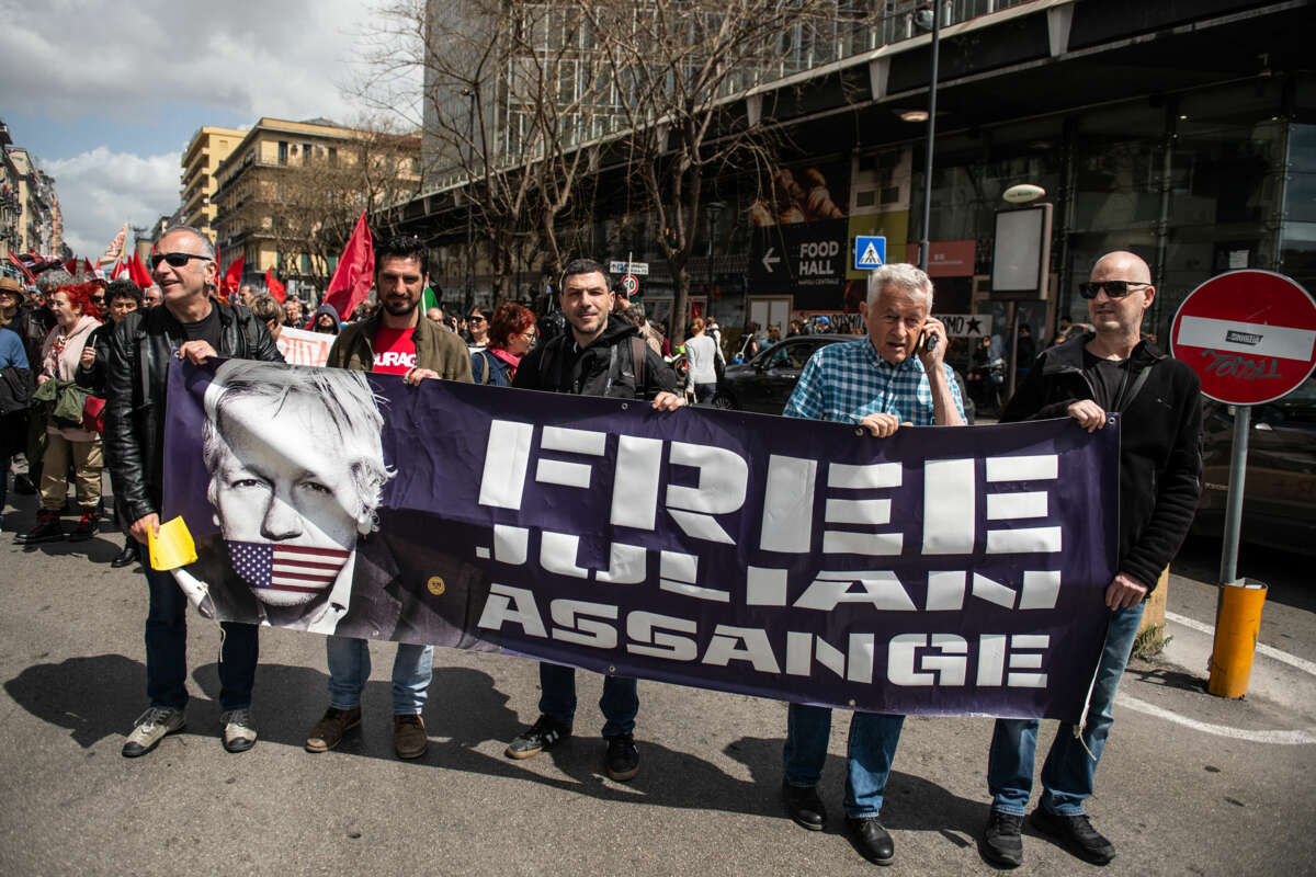 People march behind a banner displaying the face of Julian Assange alongside the words "FREE JULIAN ASSANGE" during an outdoor action