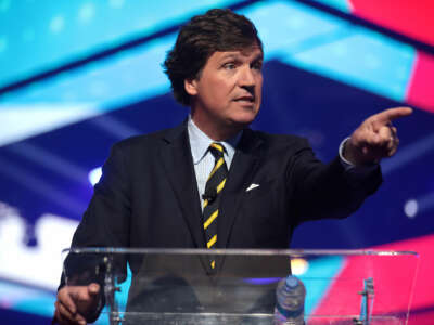 Tucker Carlson points outward while speaking at a podium