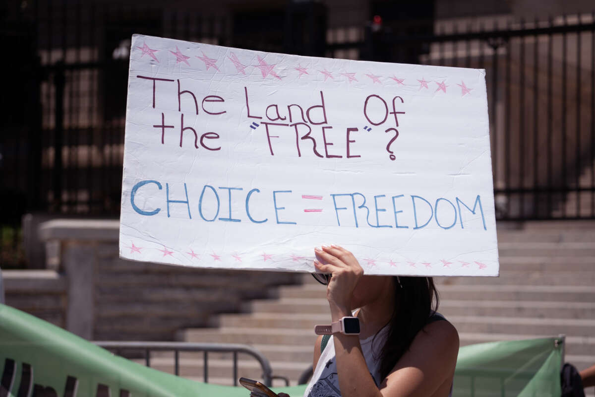 A protester holds a sign reading "THE LAND OF THE FREE? CHOICE = FREEDOM" during an outdoor protest