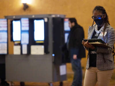A poll employee looks at a clipboard while people vote behind her