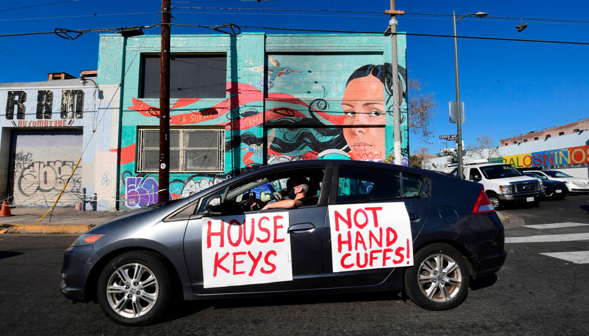 A car with "HOUSE KEYS, NOT HANDCUFFS" is seen during an outdoor protest
