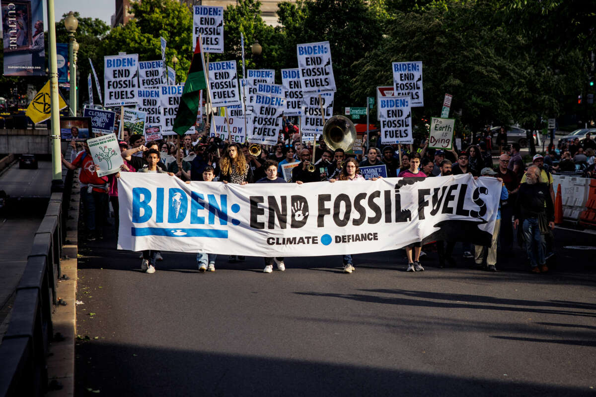 People march behind a banner reading "BIDEN: END FOSSIL FUELS" during an outdoor protest